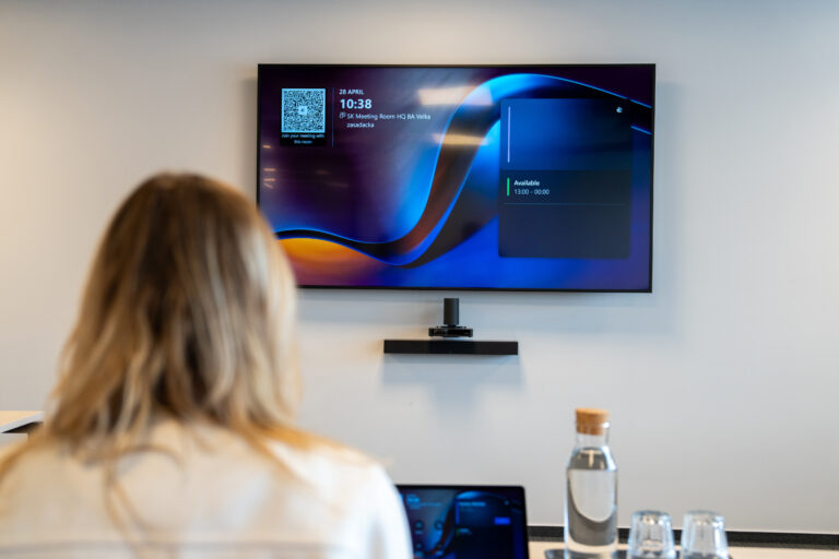 Žena v zasadačke pred obrazovkou s videolištou Yealink a dotykovým panelom na stole