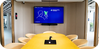 Medium meeting room with a yellow table and a Logitech video bar below the display